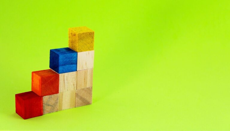 Colorful wooden blocks stacked on green background.