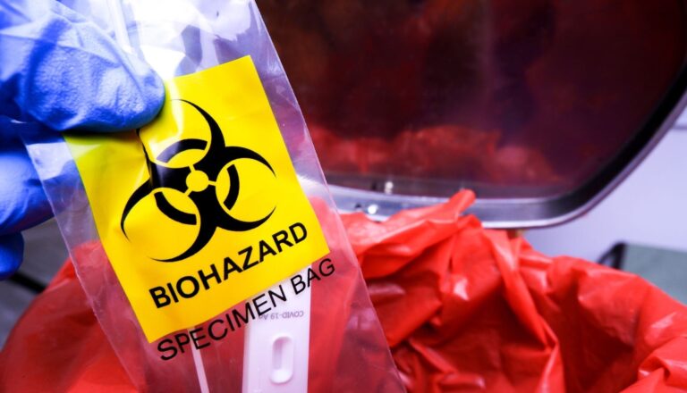 Biohazard specimen bag held beside waste container.