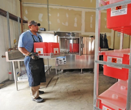 Worker manages medical waste containers in processing facility.