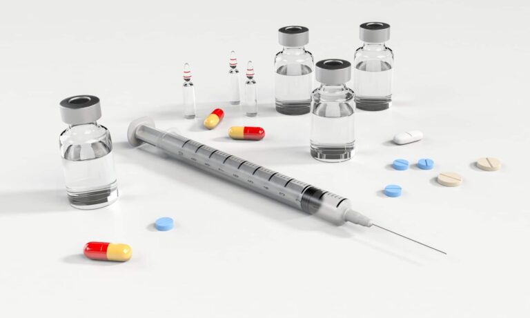 Syringe, medicine bottles, and pills on white surface.