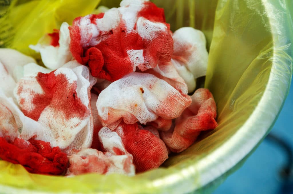 Discarded blood-soaked medical gauze in trash bin