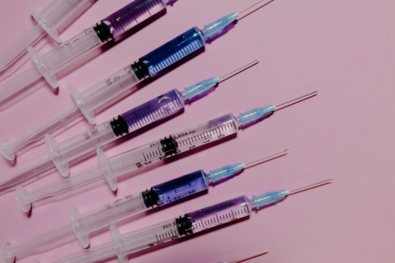 Row of medical syringes on pink background.