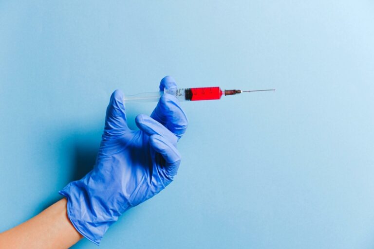 Gloved hand holding syringe with red liquid