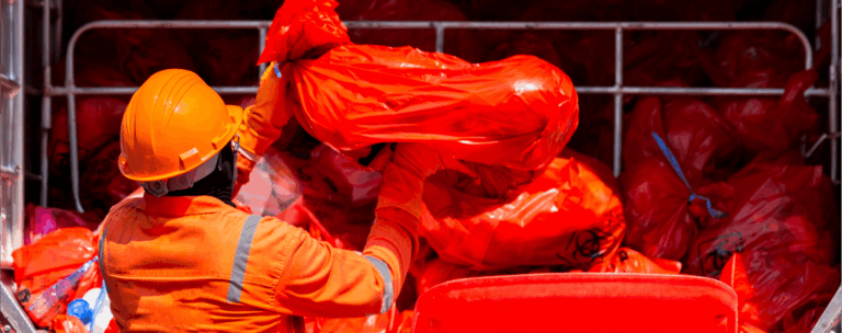 Worker handling red biohazard waste bags.