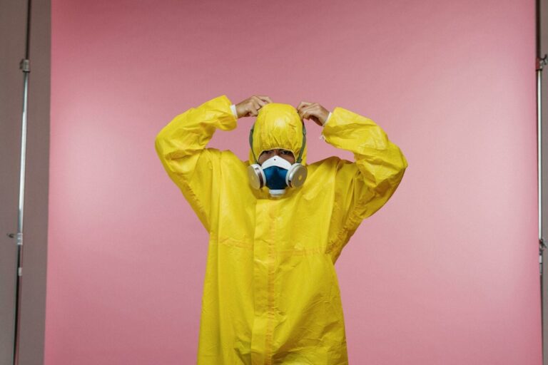 Person in hazmat suit and gas mask on pink background.