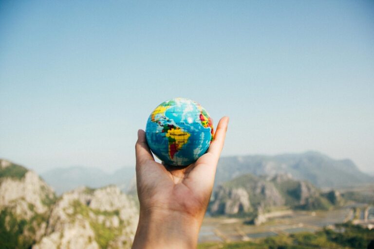 Hand holding small globe against mountain background.