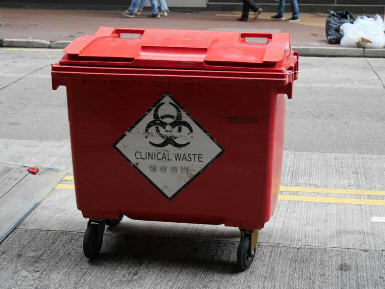 Red bin labeled clinical waste on street.