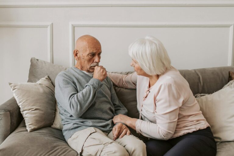 Elderly couple sitting on a sofa, comforting each other.