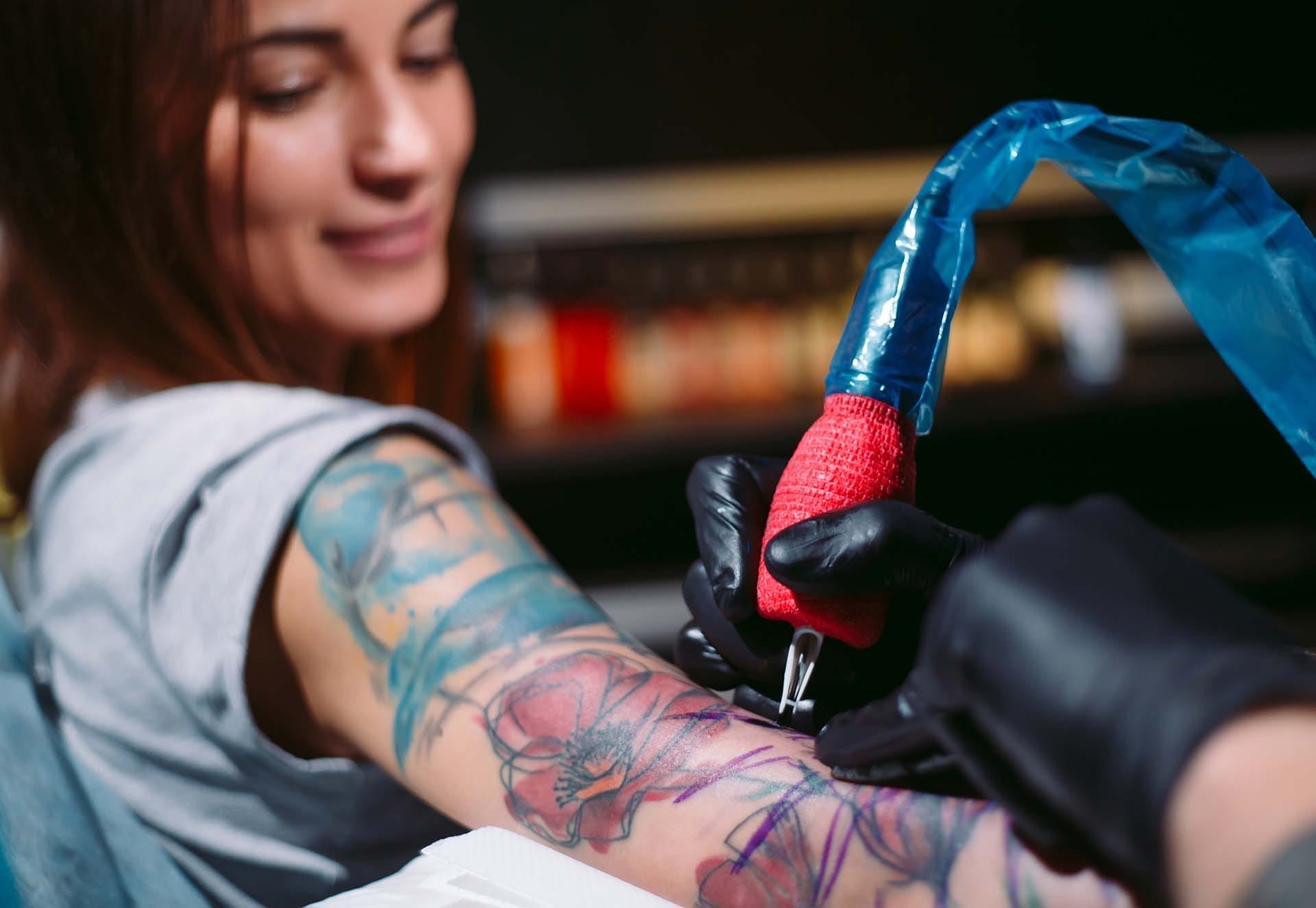 Artist tattooing colorful design on woman's arm.